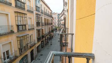 Una calle estrecha flanqueada por edificios con balcones, un escaparate visible y un cielo despejado.