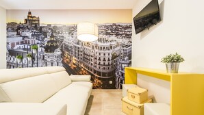A modern living room with a cityscape mural, a white sofa, a yellow console table, and a small plant. - Smartr Madrid Chueca  (Madrid)