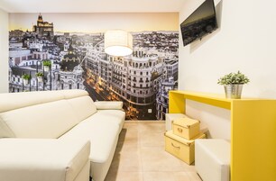 Ein modernes Wohnzimmer mit Stadtansicht-Wandbild, einem weißen Sofa, einem gelben Konsolentisch und einer kleinen Pflanze.
