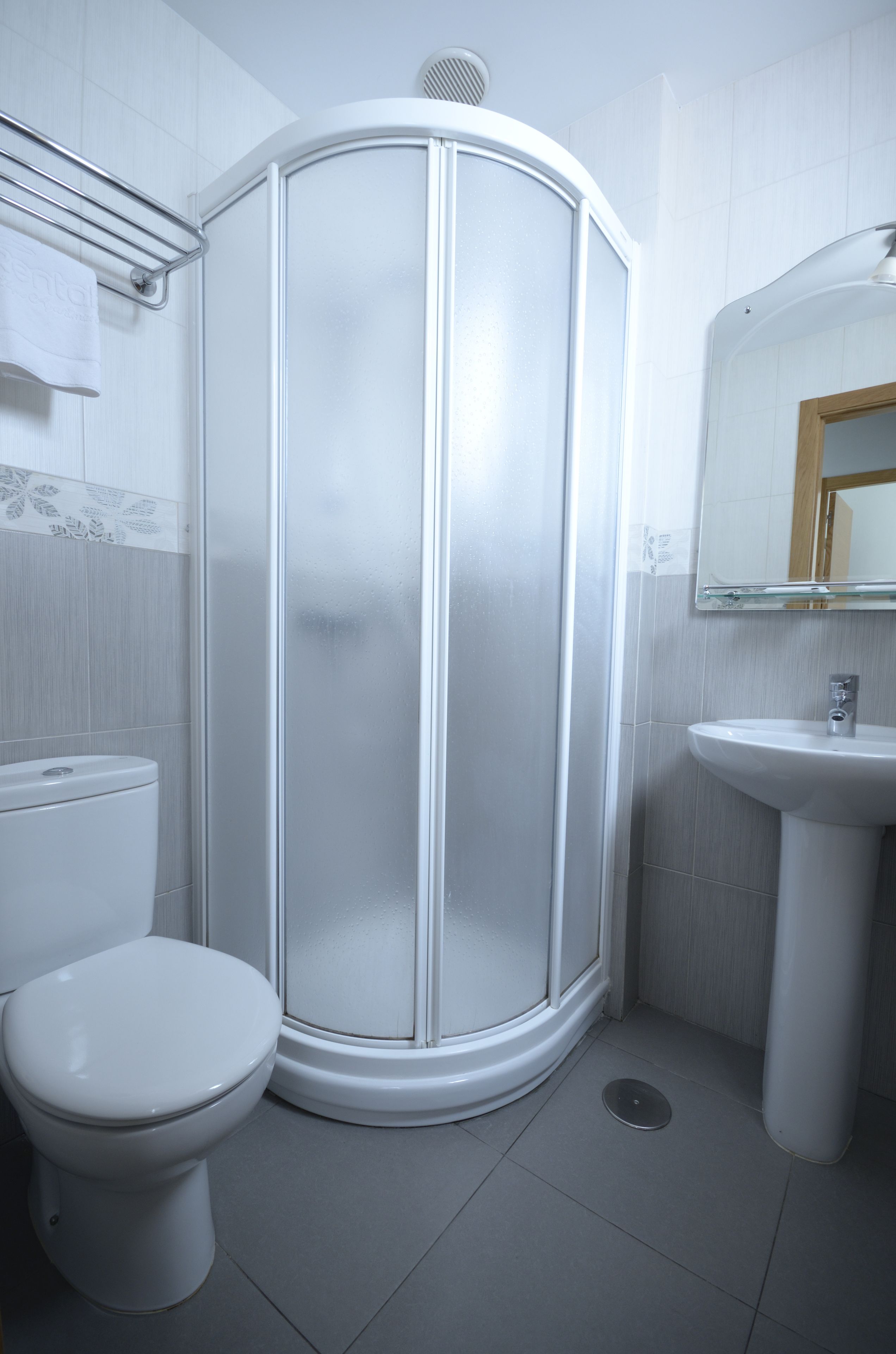 Un baño con inodoro blanco, ducha con mampara de vidrio y lavamanos con espejo.