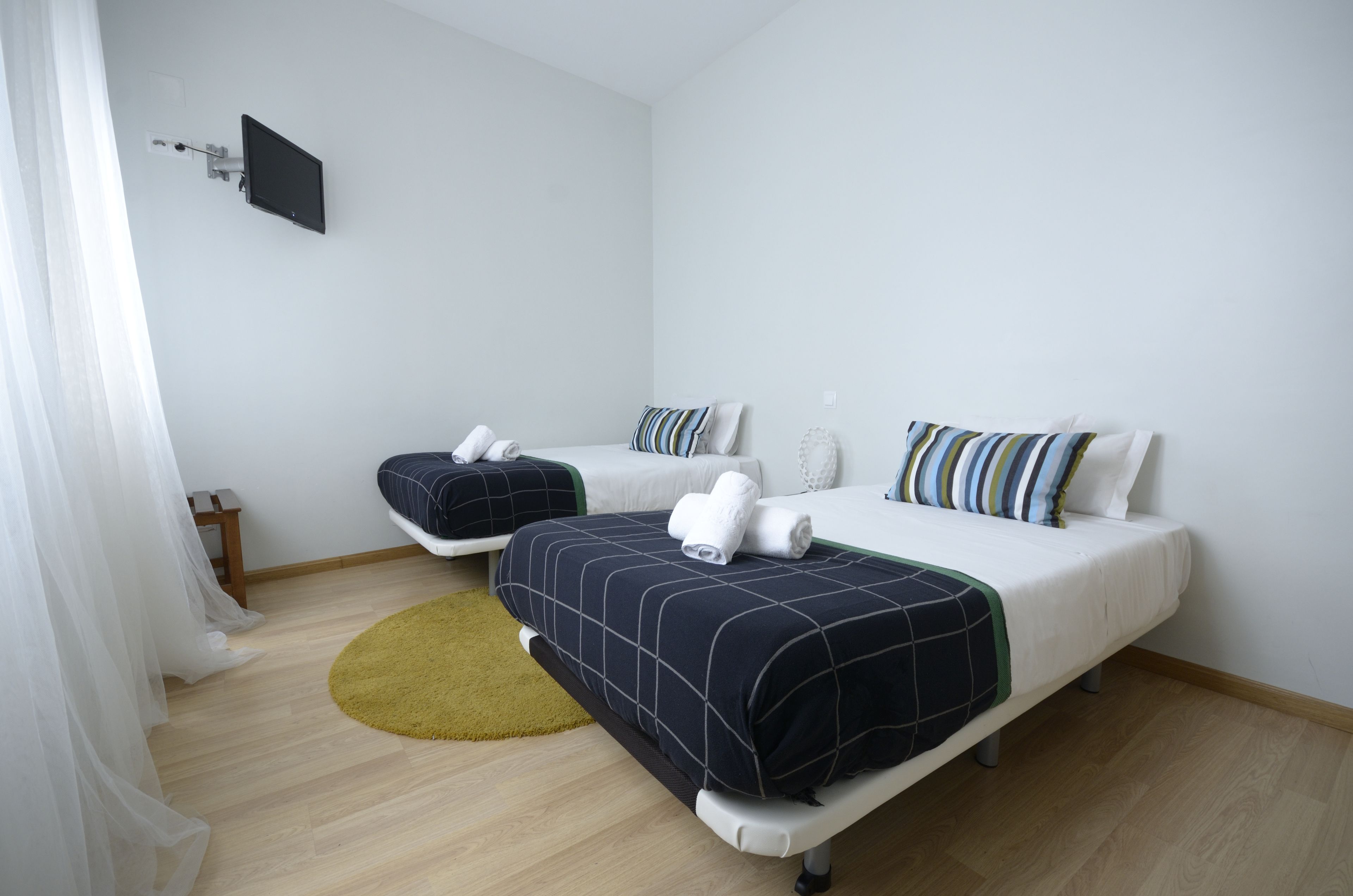 Une chambre d’hôtel avec deux lits, un téléviseur fixé au mur, une petite table en bois et un tapis rond.