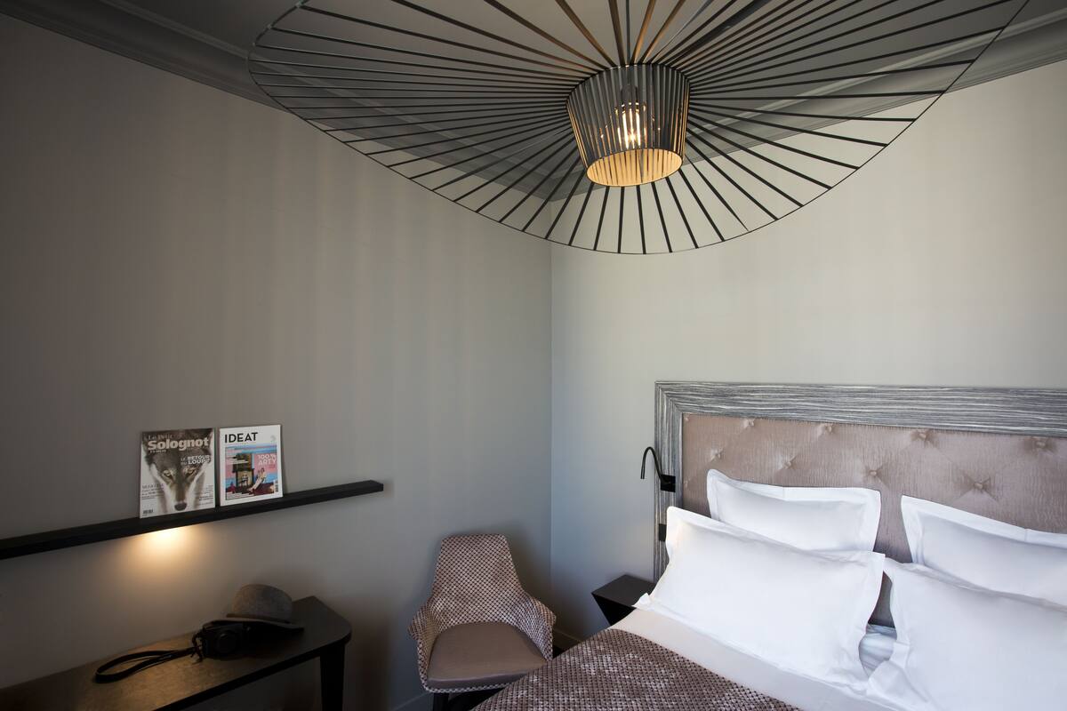 A hotel room with a bed, a chair, a nightstand, and a ceiling light fixture.