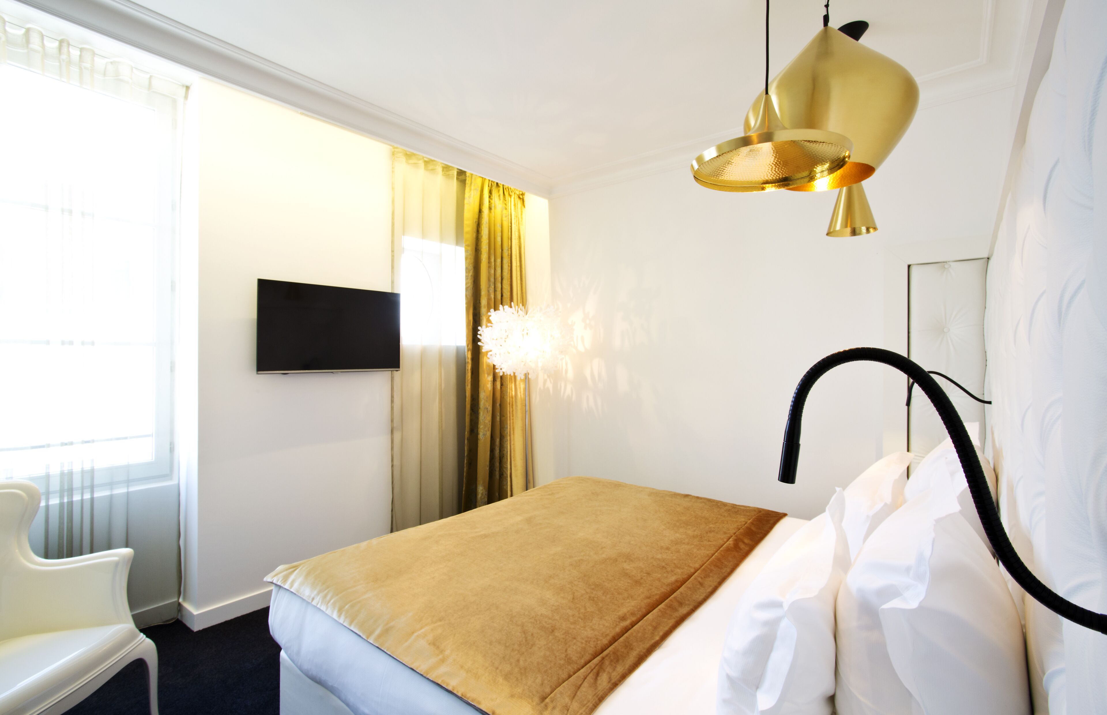 Une chambre d’hôtel avec un lit, une chaise, un téléviseur fixé au mur et une fenêtre avec des rideaux.