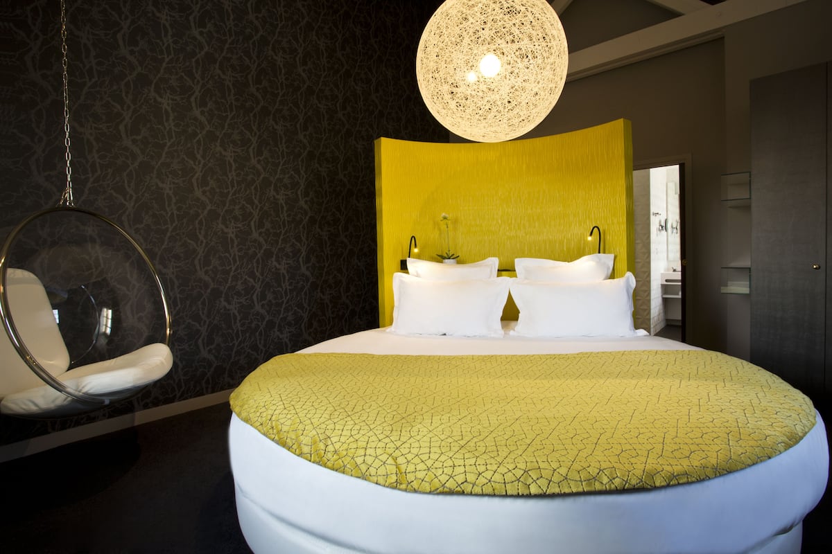A modern hotel room with a large bed, a hanging chair, and a unique textured light fixture.
