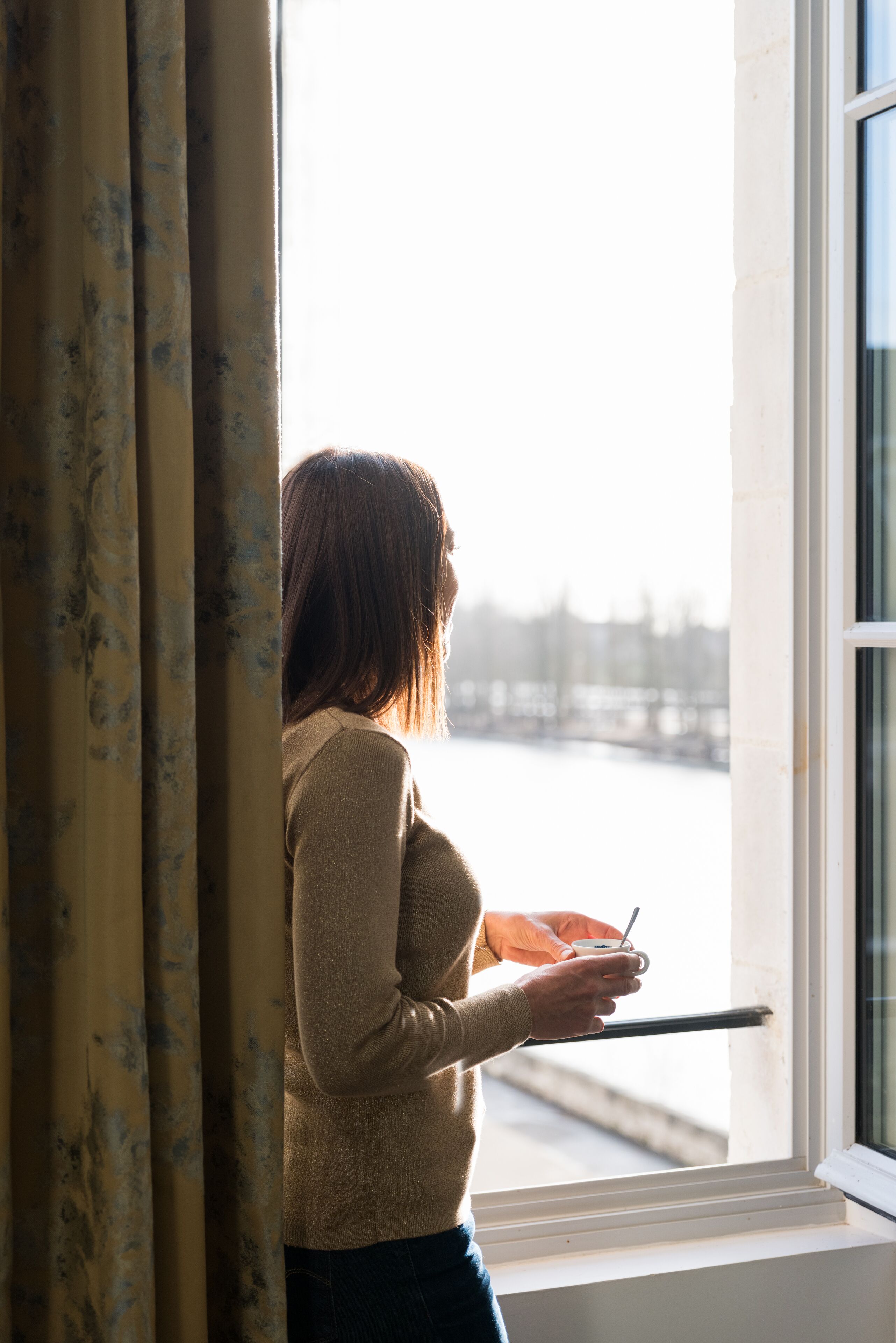A person standing by a window with a view of a body of water and buildings.