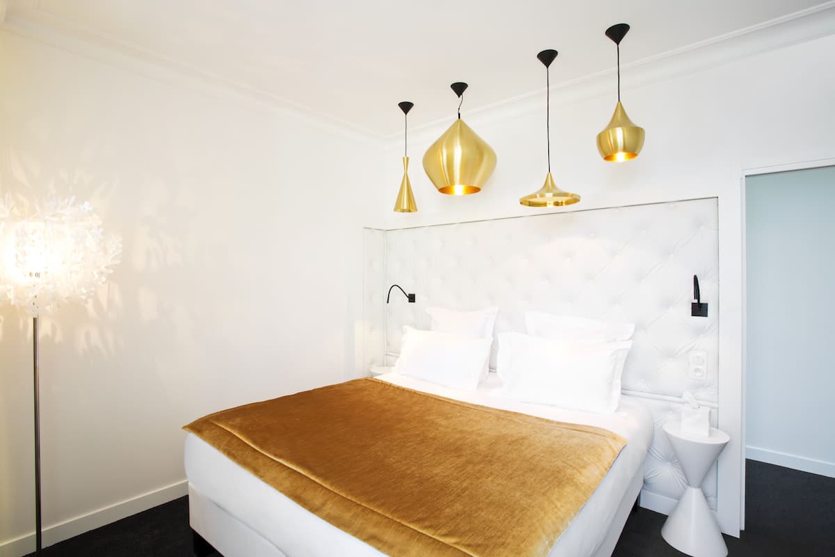 A modern hotel room with a large bed, a gold throw blanket, and three pendant lights.