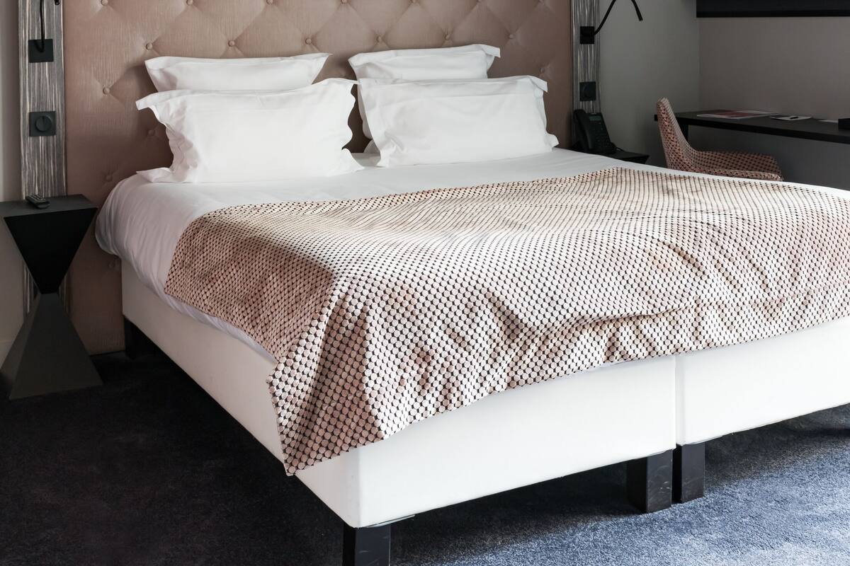 A neatly made bed with a patterned bedspread, a tufted headboard, and three pendant lights above.