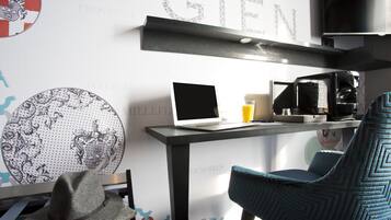 Una habitación moderna con un ordenador portátil sobre un escritorio, una cafetera y una silla azul.