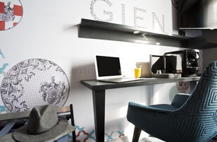 Una habitación moderna con un ordenador portátil sobre un escritorio, una cafetera y una silla azul.