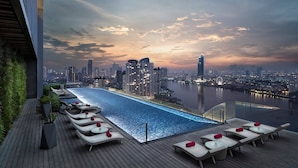 A rooftop infinity pool with lounge chairs and a city skyline view at dusk. - Avani+ Riverside Bangkok Hotel (Bangkok)