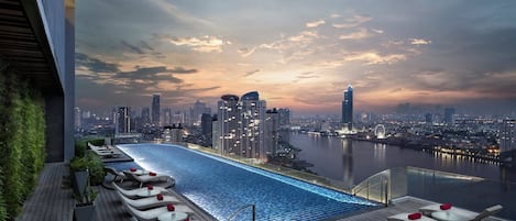 Une piscine à débordement située sur le toit, avec des chaises longues et une vue sur les toits de la ville au crépuscule.