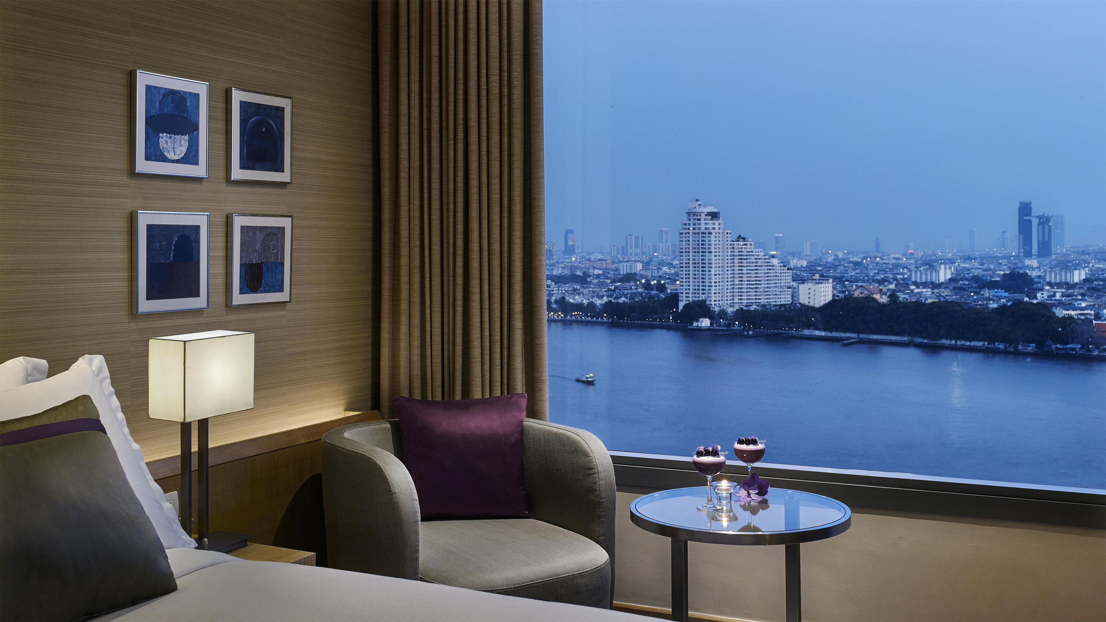 Quarto de hotel com vista para a cidade, uma cama, uma cadeira, uma mesa com bebidas e quadros na parede.