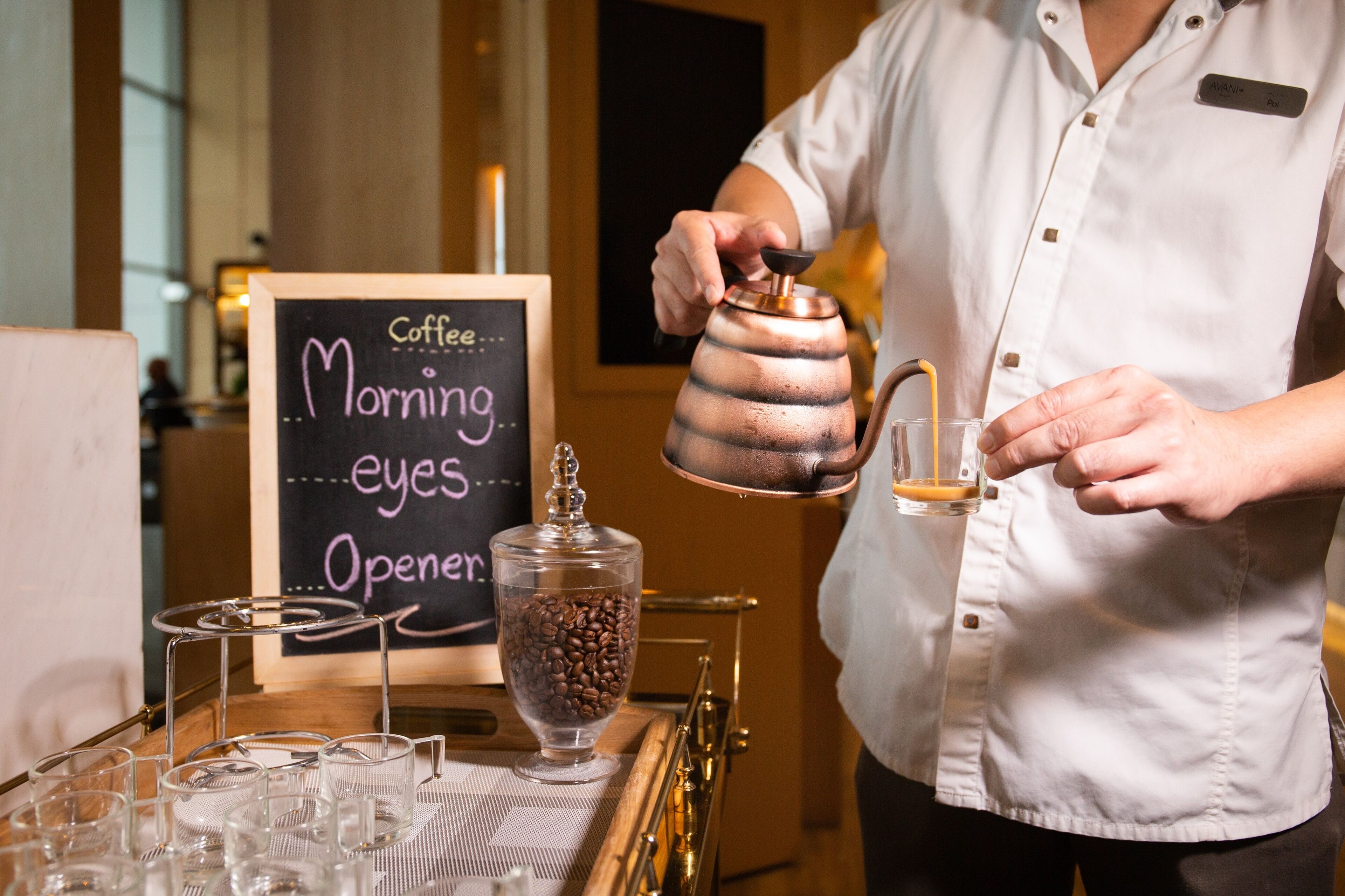 Un barista prepara café en una cafetería con un cartel de pizarra que dice 