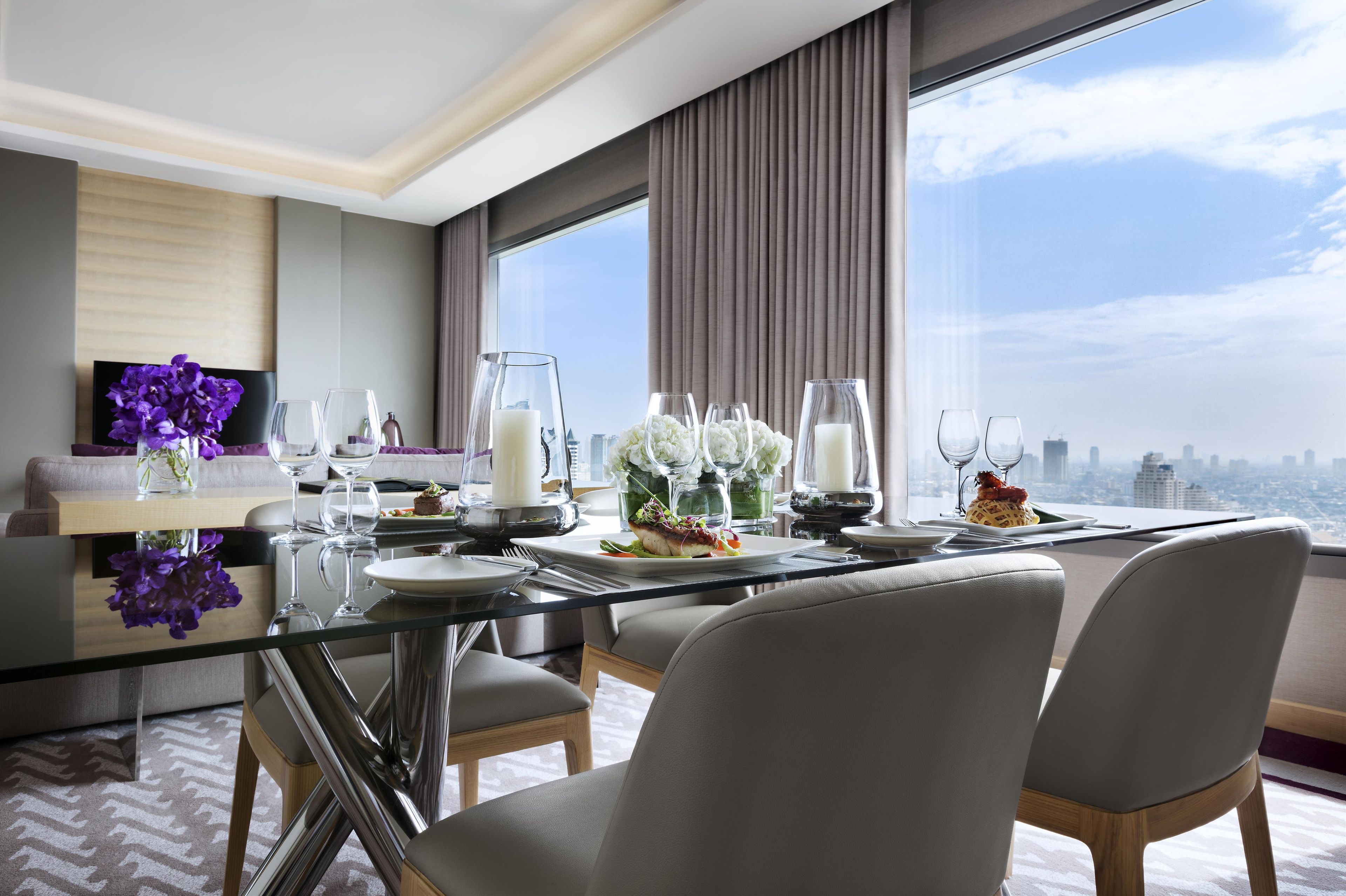 Un comedor moderno con una mesa de vidrio, sillas tapizadas de color gris y vistas a la ciudad.