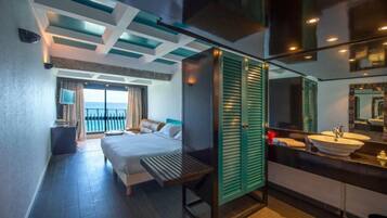Une chambre d’hôtel moderne équipée d’un lit, d’un bureau, d’une salle de bain avec un lavabo et un miroir, et offrant une vue sur la mer.