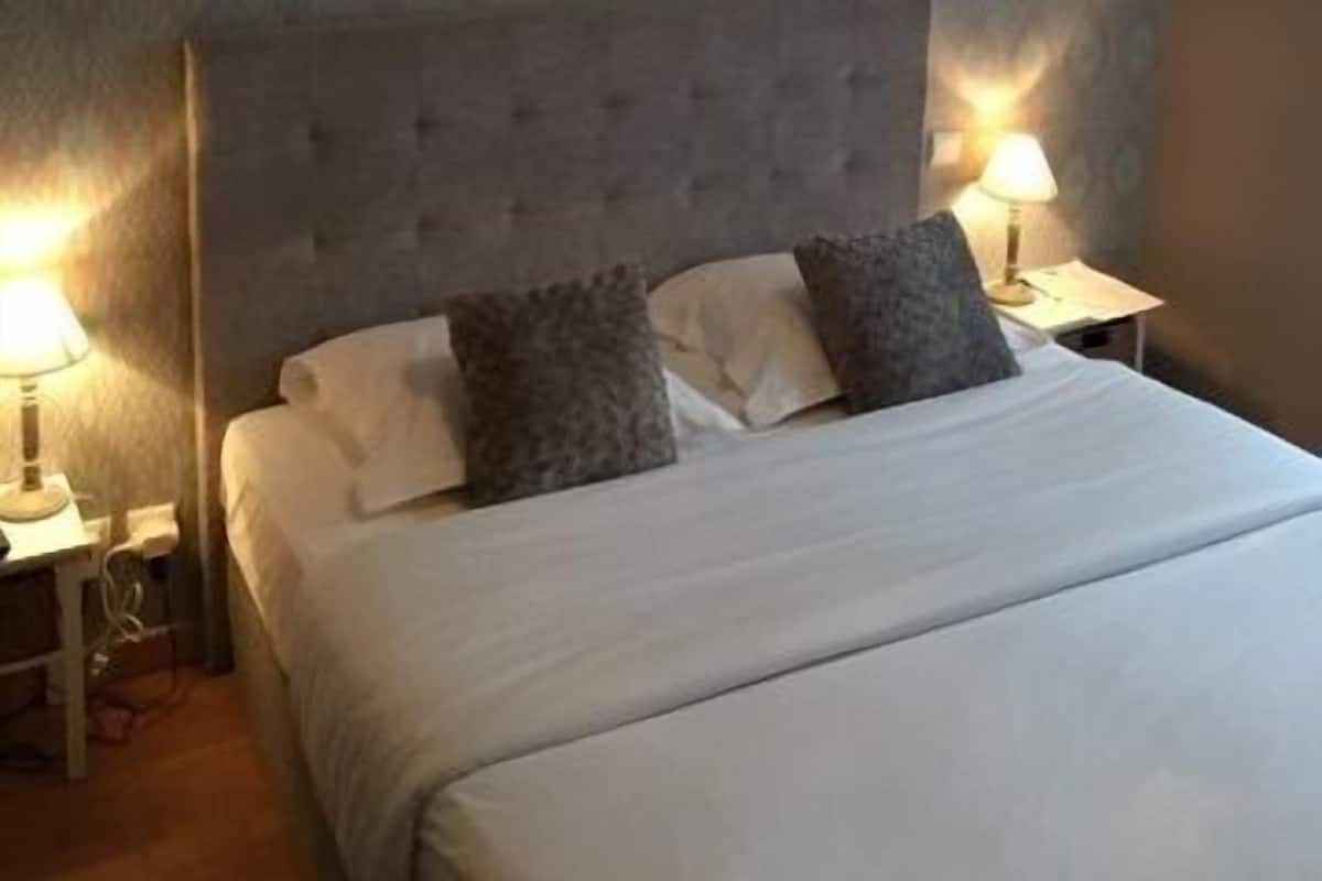 A bedroom with a large bed, two bedside tables, and a hanging lamp.