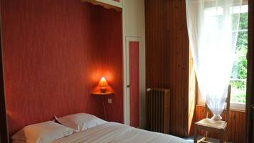 A bedroom with a bed, a chair, a wall-mounted lamp, and a window with a sheer curtain.