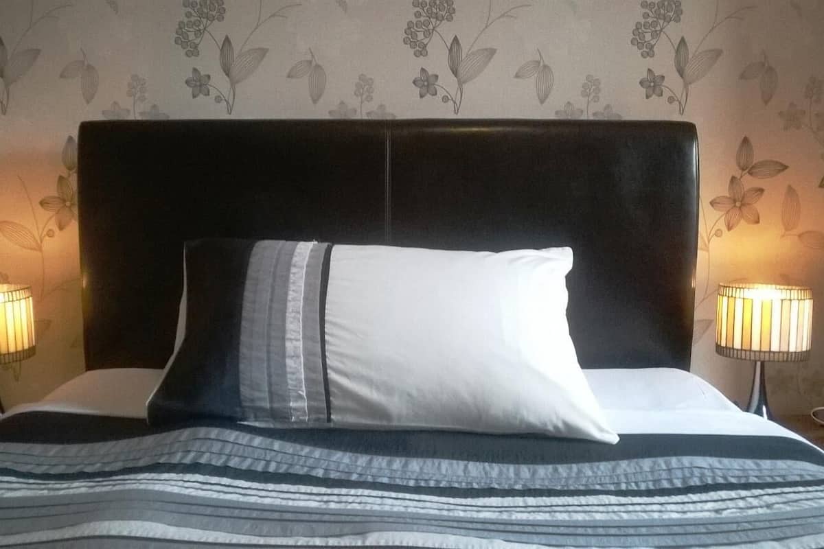 A neatly made bed with a dark headboard, two bedside lamps, and floral wallpaper.