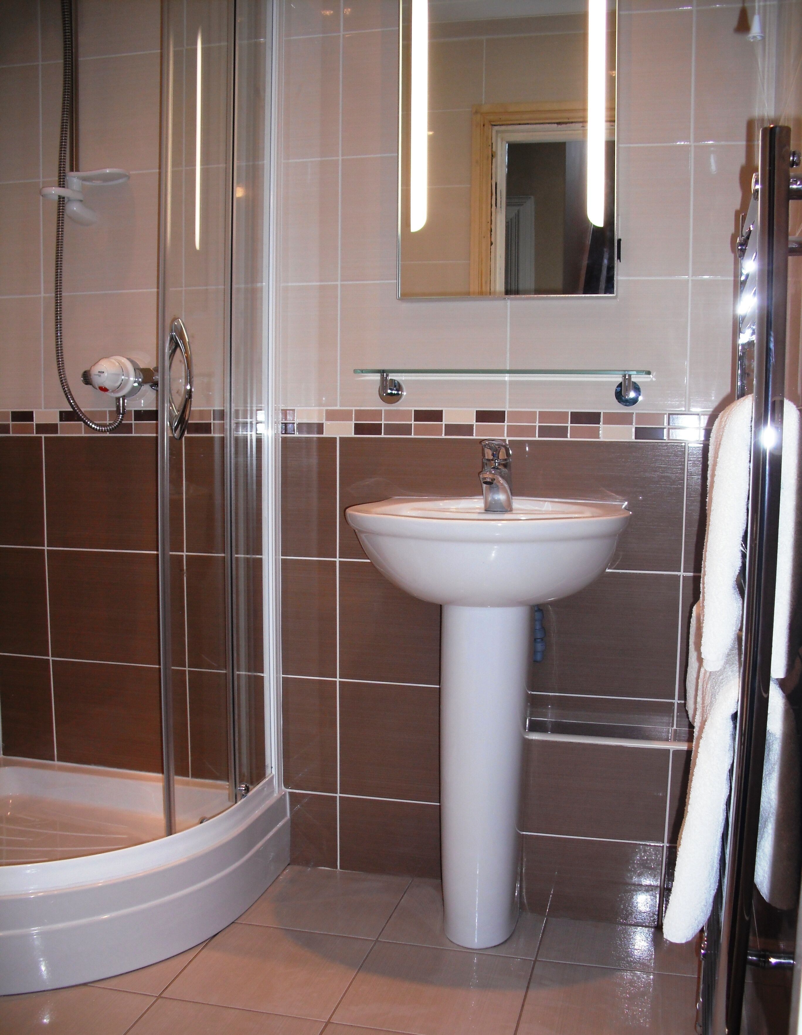A bathroom with a glass shower enclosure, a white sink, and a mirror above the sink.