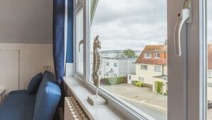Ein Zimmer mit einem Bett, einem Fenster mit Blick auf Häuser und einer Statue an der Fensterbank.
