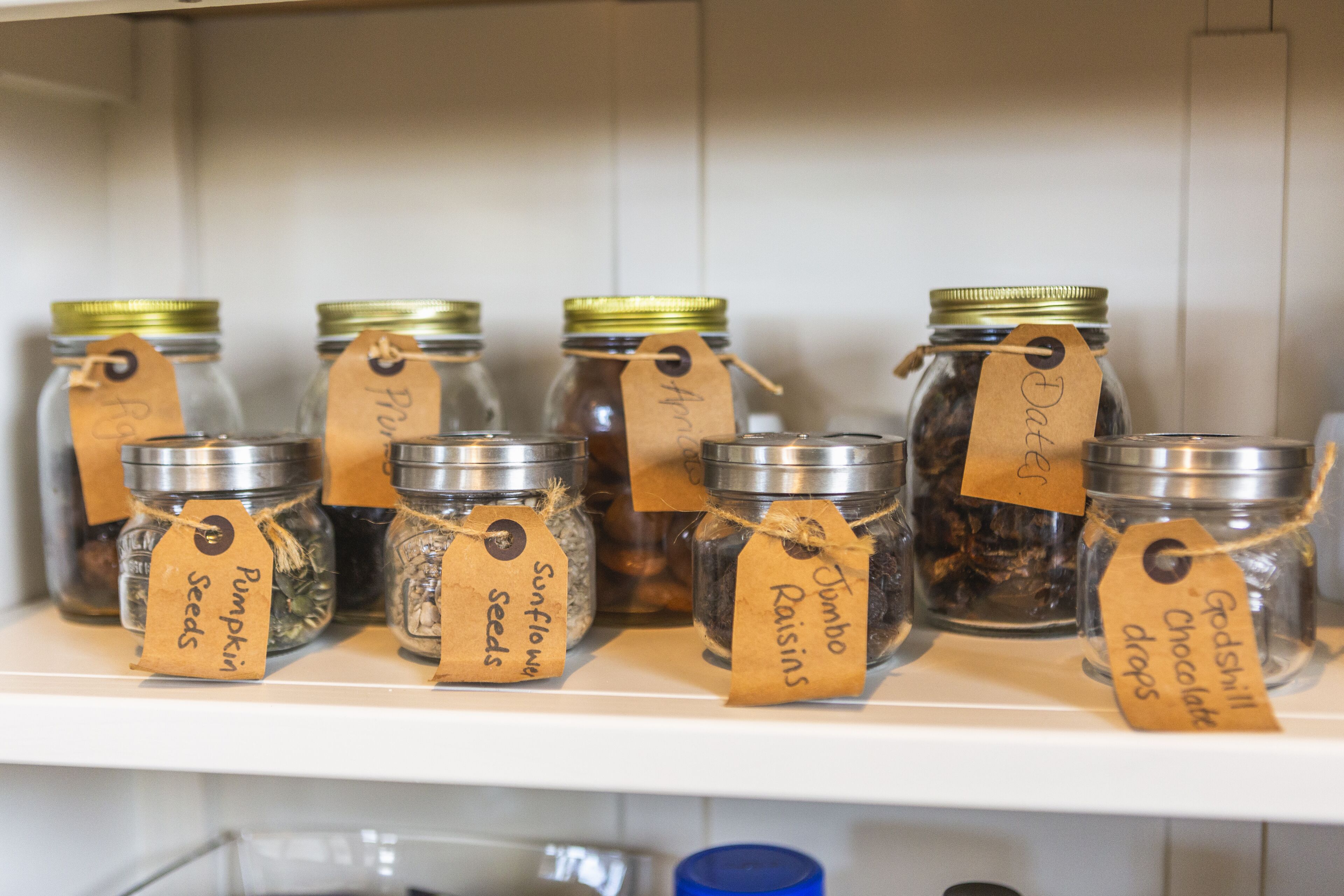 A shelf with jars labeled with various contents like seeds, sunflowers, and chocolate drops.