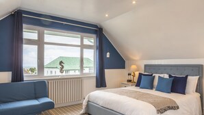Ein Schlafzimmer mit einem großen Bett, einem blauen Sofa, einem Fenster mit Vorhängen und Blick auf ein Gebäude.