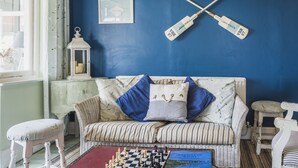 Ein gemütliches Zimmer mit blauer Wand, einem Korbssessel mit gestreiften Kissen, einem Schachbrett auf dem Boden und einem kleinen weißen Hocker.