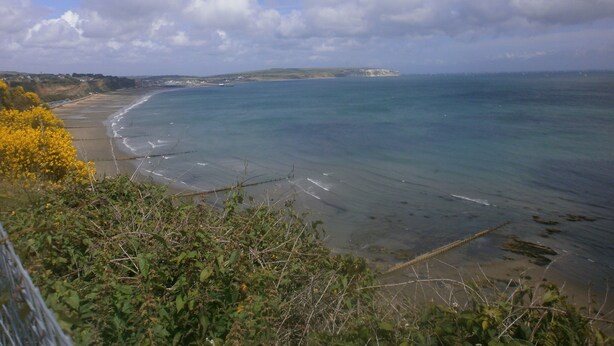 Eine Küstenlandschaft mit Sandstrand, klarem, blauem Meer und einer fernen Klippe.
