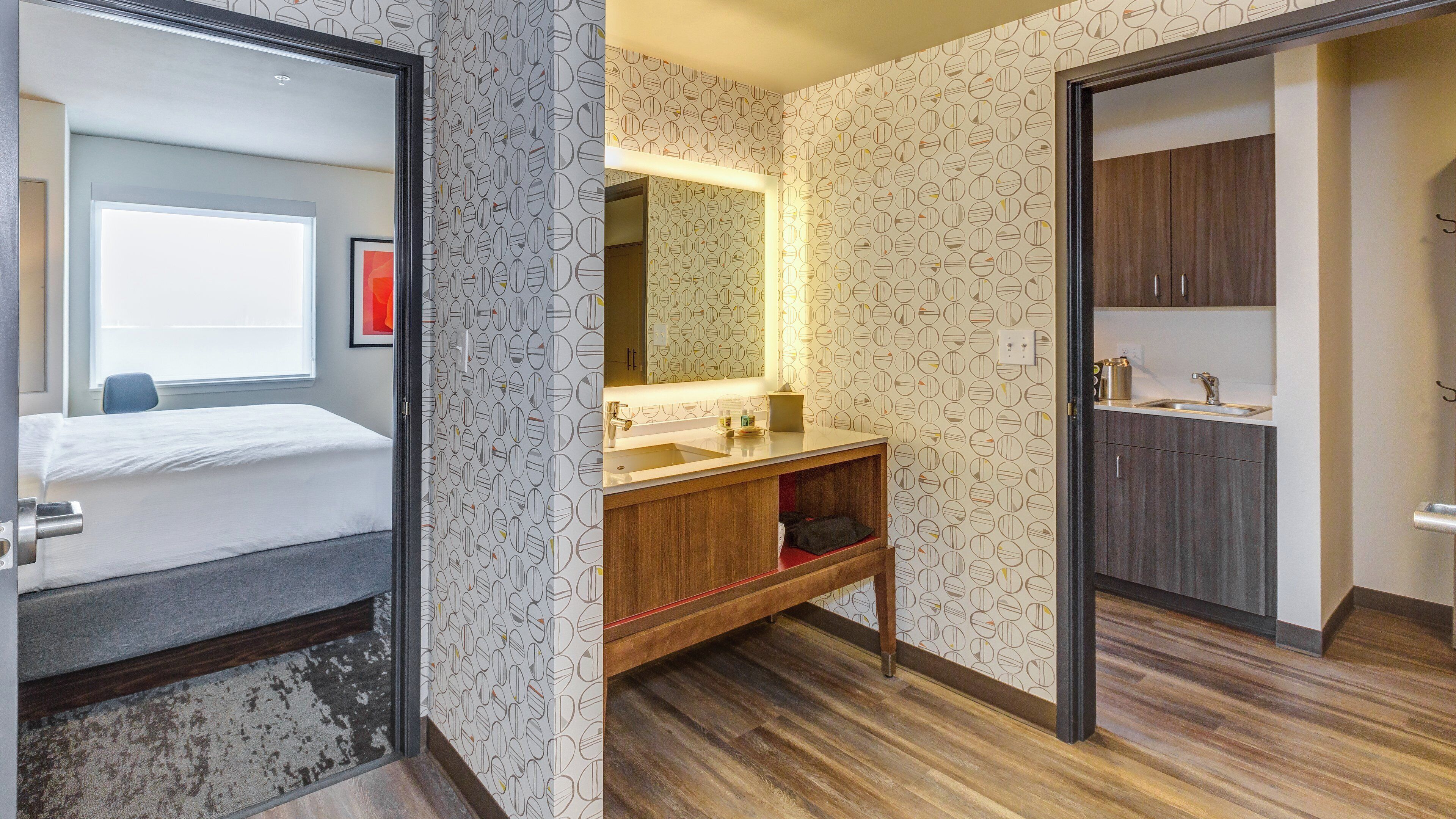 Een hotelkamer met een bed, een badkamer met een wastafel en spiegel, en een houten vloer.