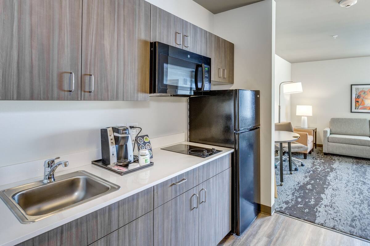 Una cocina moderna con microondas, refrigerador y cafetera integrados. Cuenta con un lavamanos y grifo, además de un comedor con mesa y sillas.