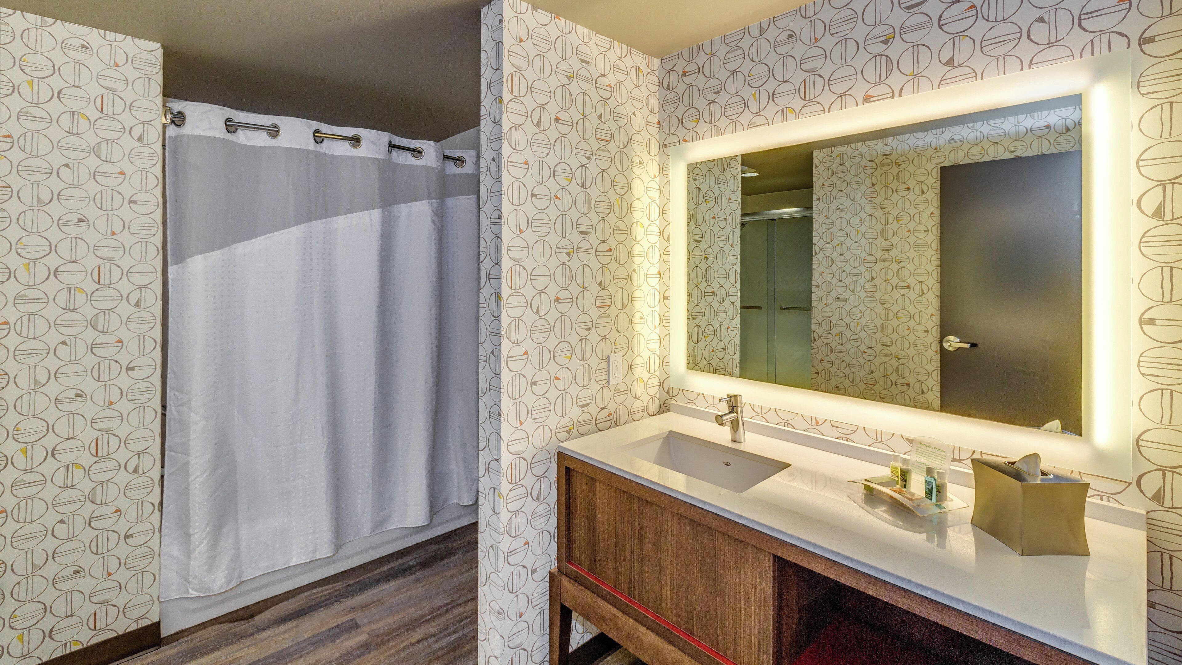 Un bany amb cortina de dutxa, un lavabo amb mirall i paper pintat.