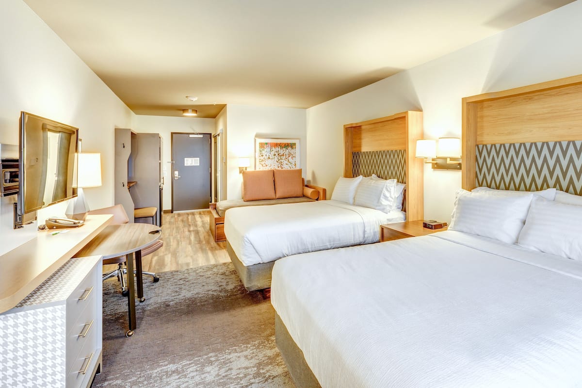Una habitación de hotel con dos camas, un escritorio, una silla, un espejo y una puerta.