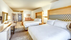 A hotel room with two beds, a desk, a chair, a mirror, and a door.