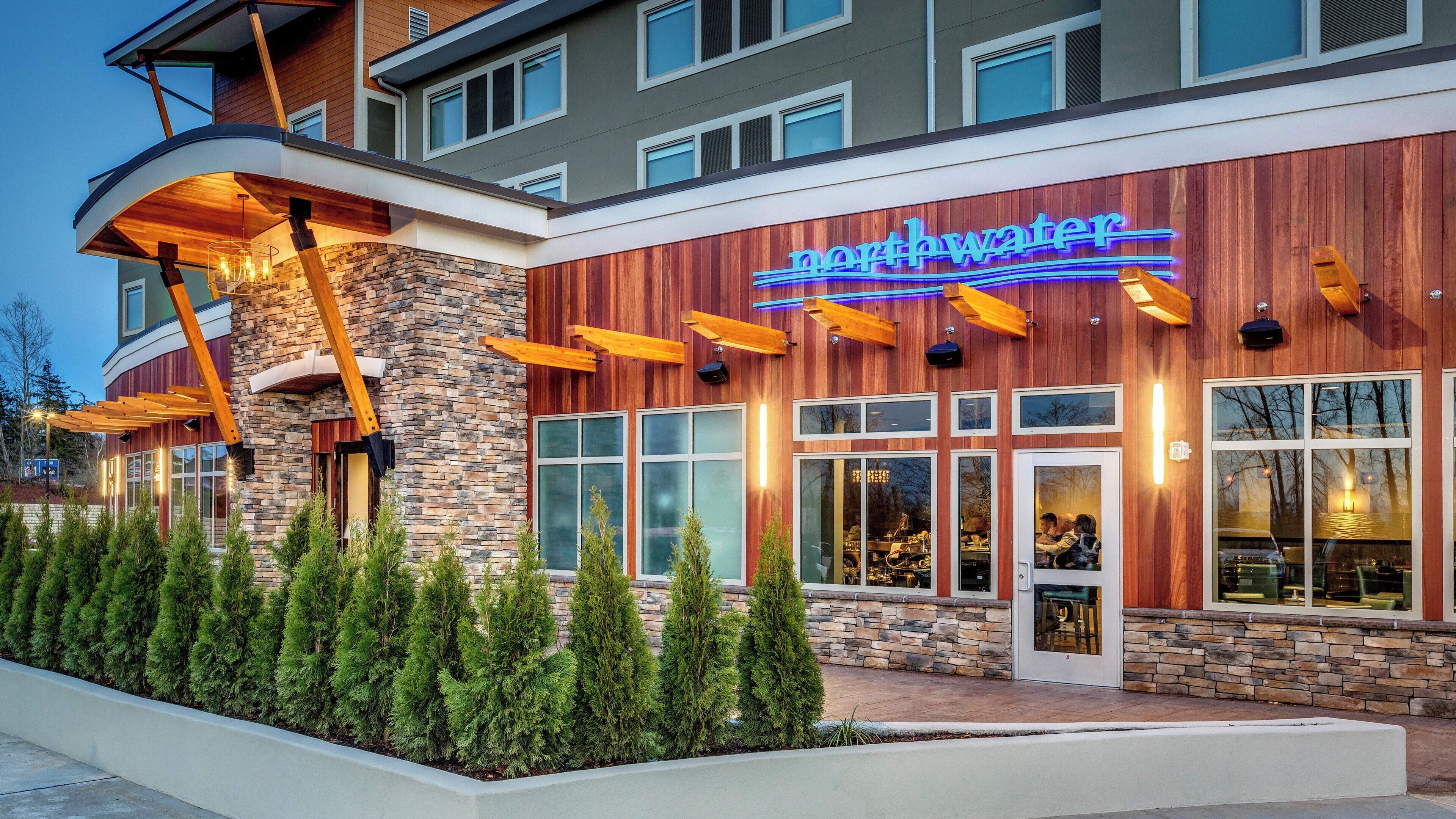 A modern building with a stone facade, large windows, and a neon sign.