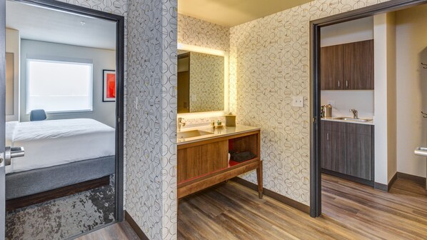 A hotel room with a bed, a bathroom with a sink and mirror, and a wardrobe.