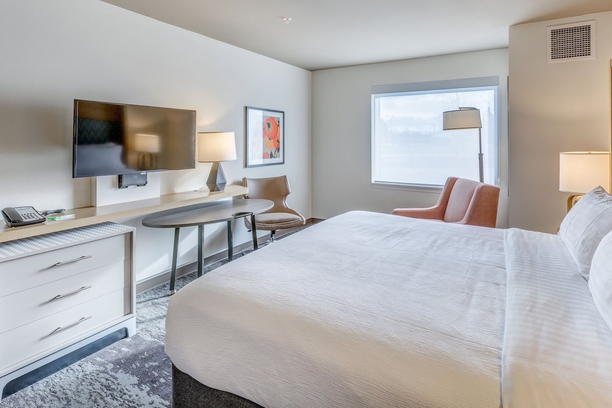 Habitación de hotel con una cama grande, un escritorio con teléfono, una silla, televisión y ventana con vista al cielo.