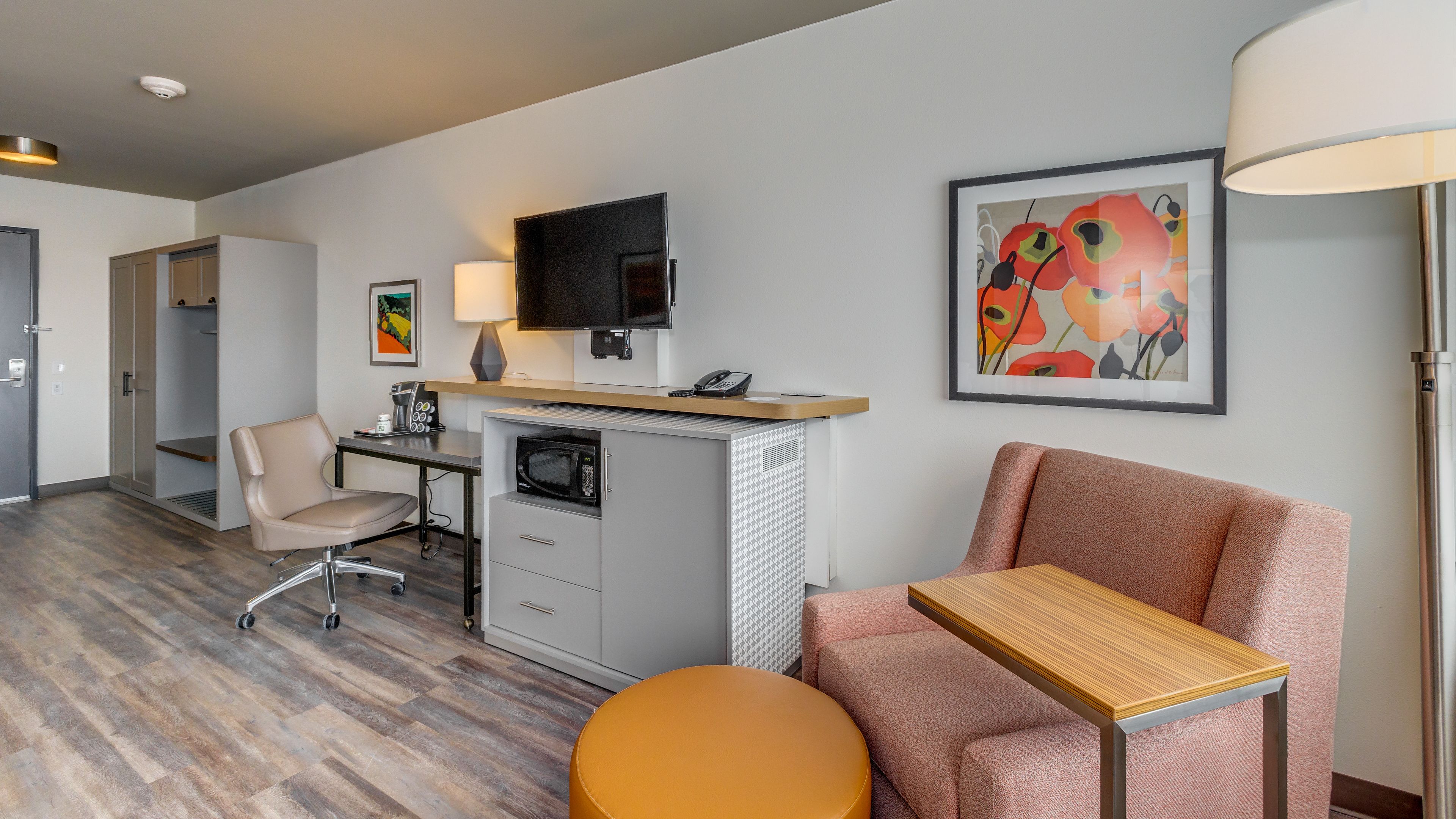 Een hotelkamer met een bureau, een stoel, een bank, een magnetron, een televisie en kunst aan de muren.
