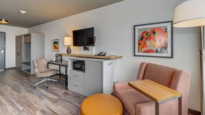 A hotel room with a desk, a chair, a sofa, a microwave, a television, and artwork on the walls.