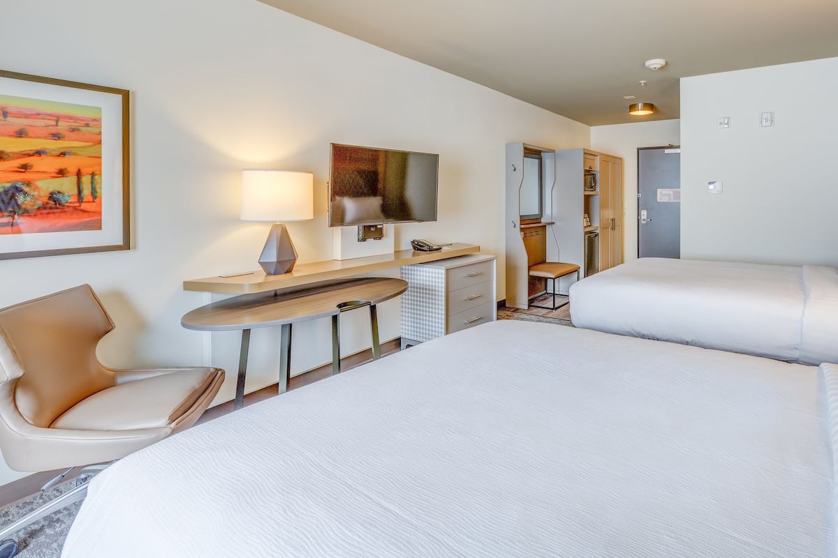 Una habitación de hotel con una cama grande, un escritorio con silla, un televisor y un cuadro en la pared.