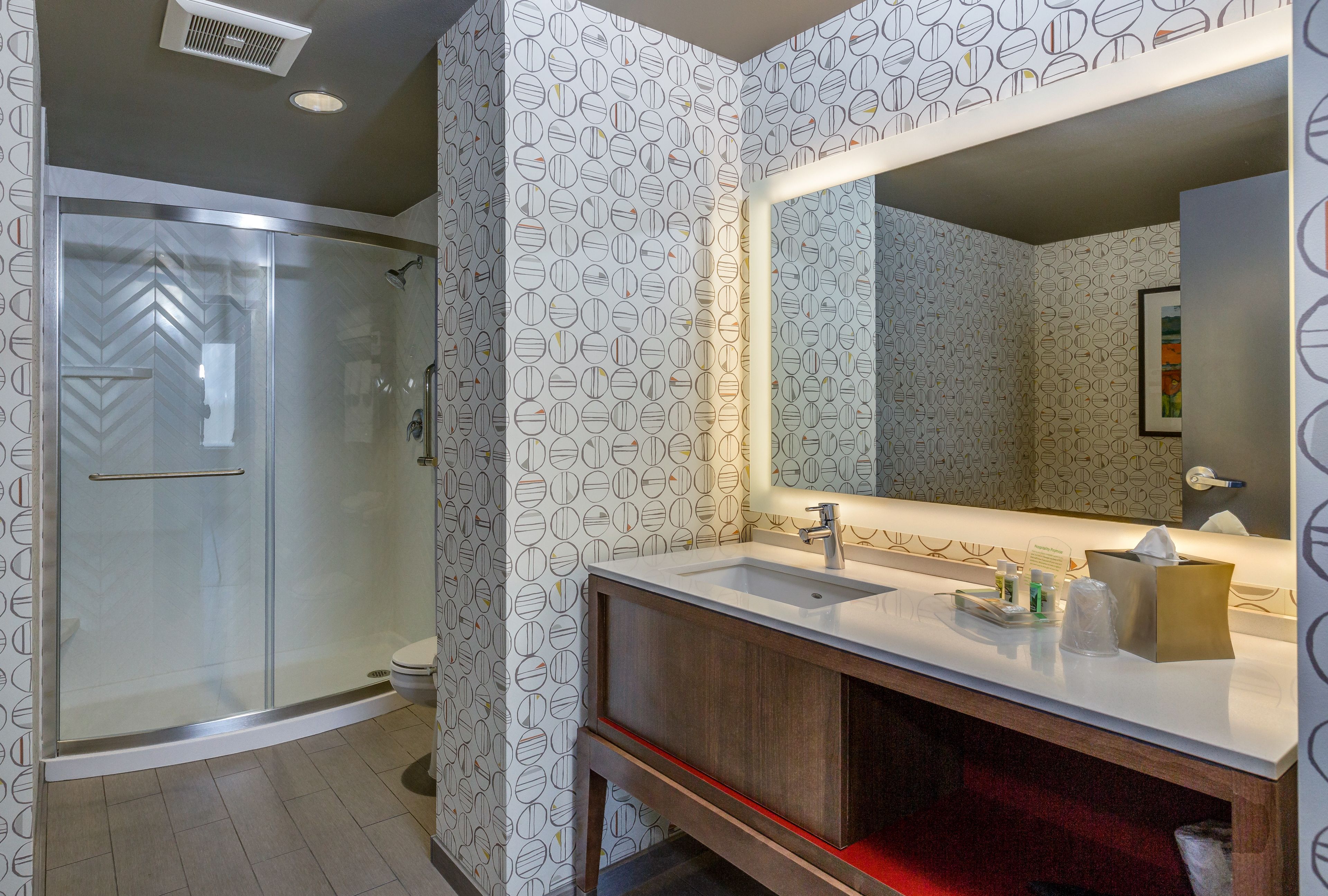 A modern bathroom with a glass-enclosed shower, a large mirror, and a vanity with a sink.