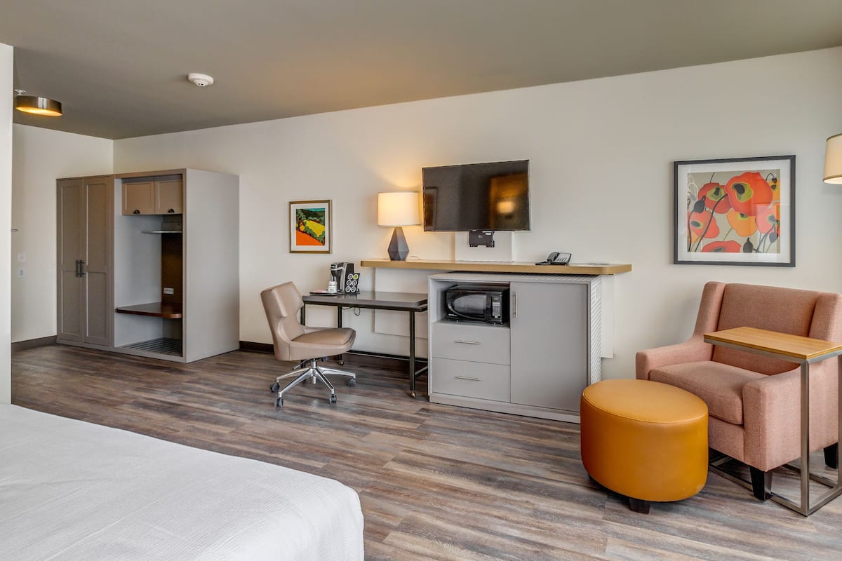 Habitación de hotel con cama, escritorio con computadora, silla, microondas, cafetera y televisión.