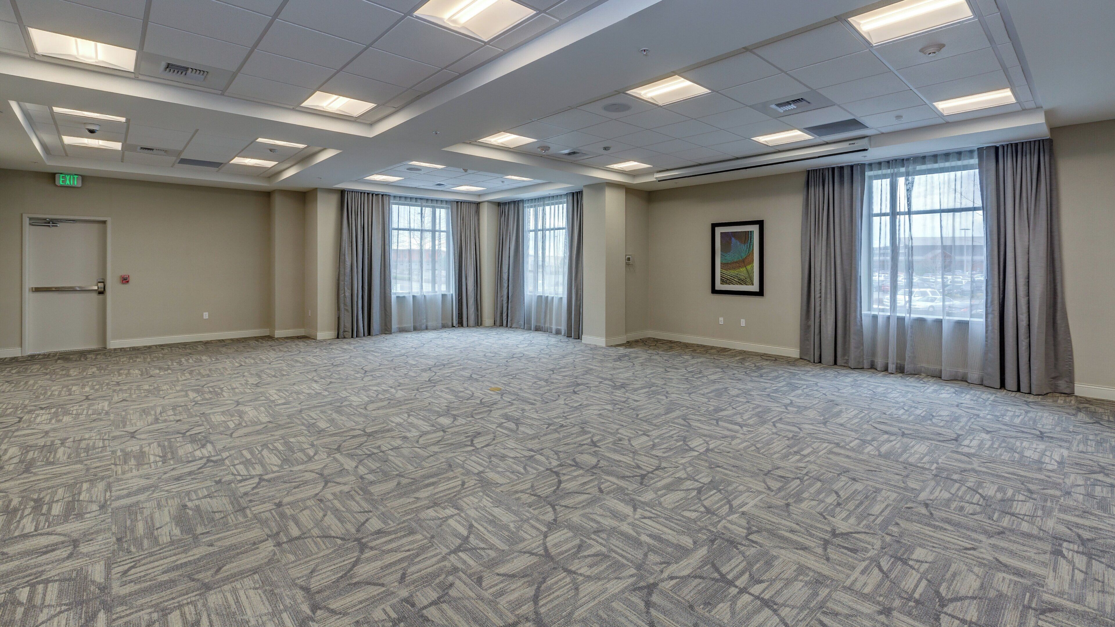 Un salón de conferencias amplio y vacío con alfombra estampada, una puerta y ventanas con cortinas.