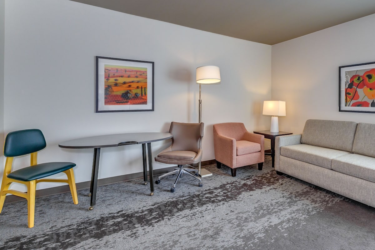 Habitación de hotel con sofá, dos sillones, una mesa, una lámpara de pie y dos cuadros en las paredes.