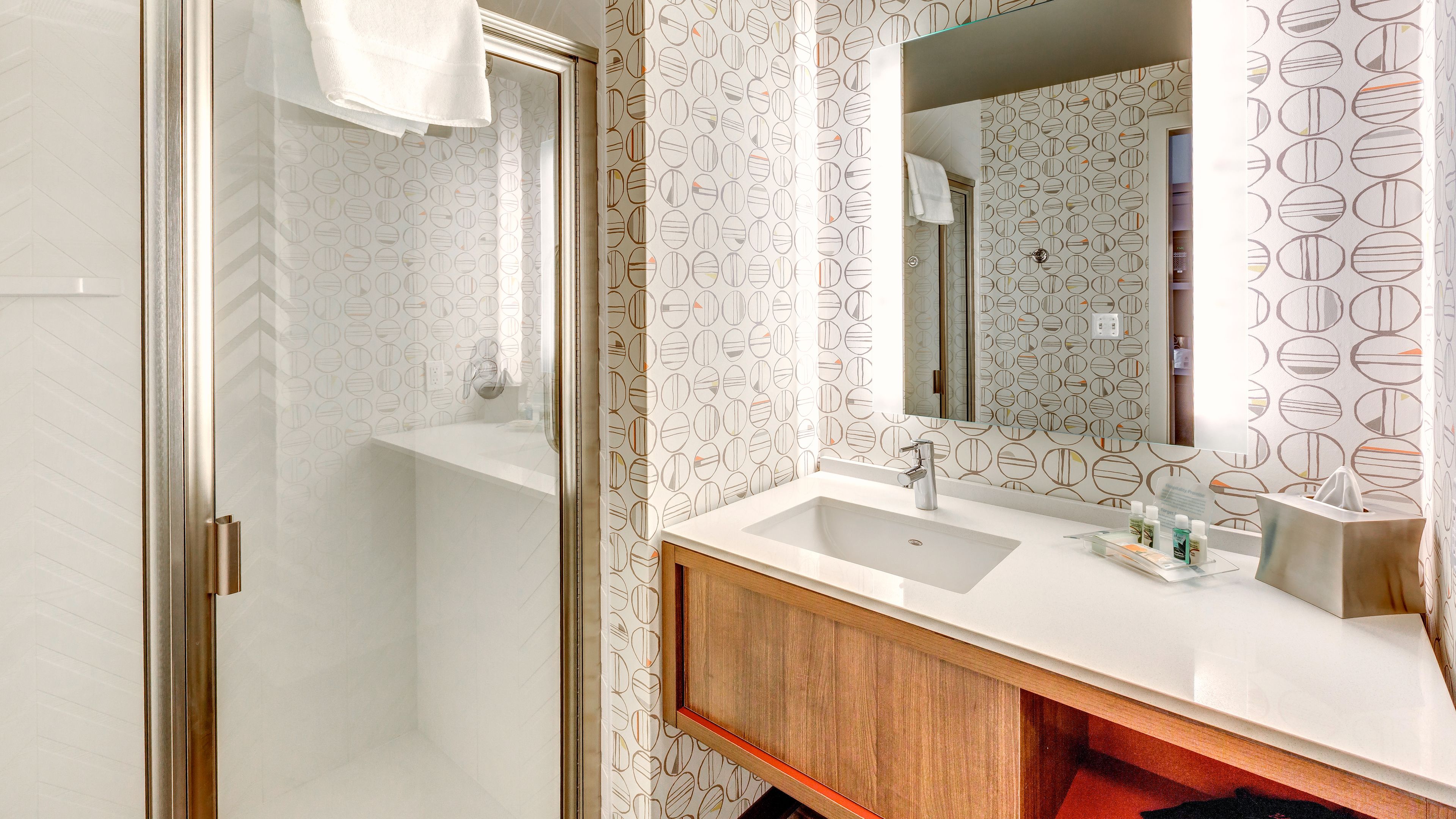A modern bathroom with a white sink, wooden vanity, and a large mirror.