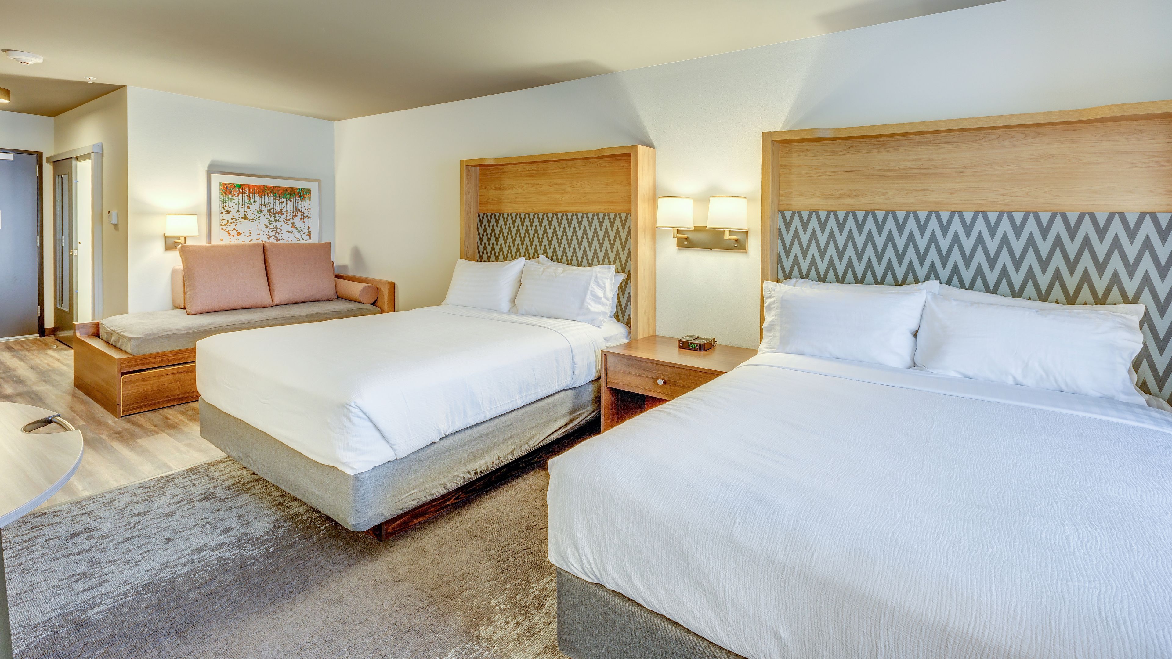 Une chambre d’hôtel avec deux lits, un canapé, une tête de lit en bois, des lampes de chevet et un tapis.