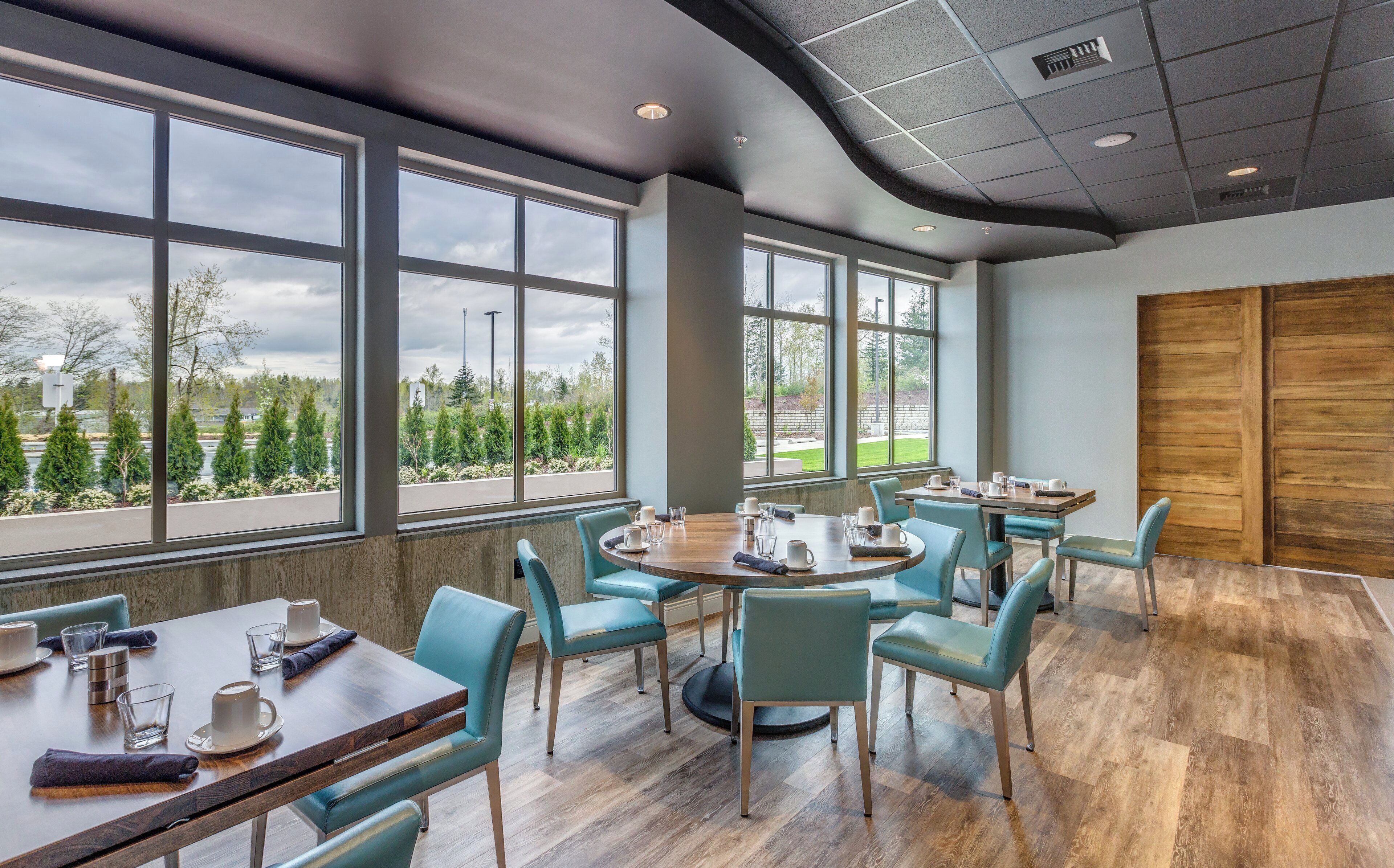A modern conference room with large windows, wooden flooring, and teal chairs.