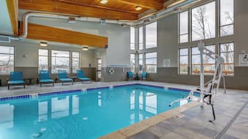 An indoor swimming pool with clear blue water, wooden ceiling beams, and large windows.