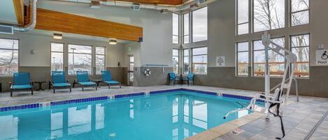 An indoor swimming pool with clear blue water, wooden ceiling beams, and large windows.