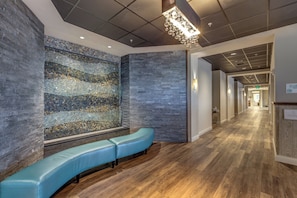 A modern lobby with a stone wall, a blue bench, and a wooden floor.