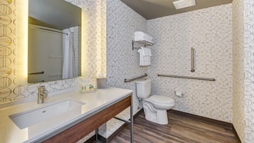 A bathroom with a white sink, mirror, and toilet. There are handrails and a towel rack. The walls have a circular pattern.